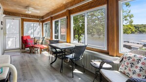 Une véranda avec un plafond en bois, de grandes fenêtres, une table avec des chaises et une vue sur un lac.