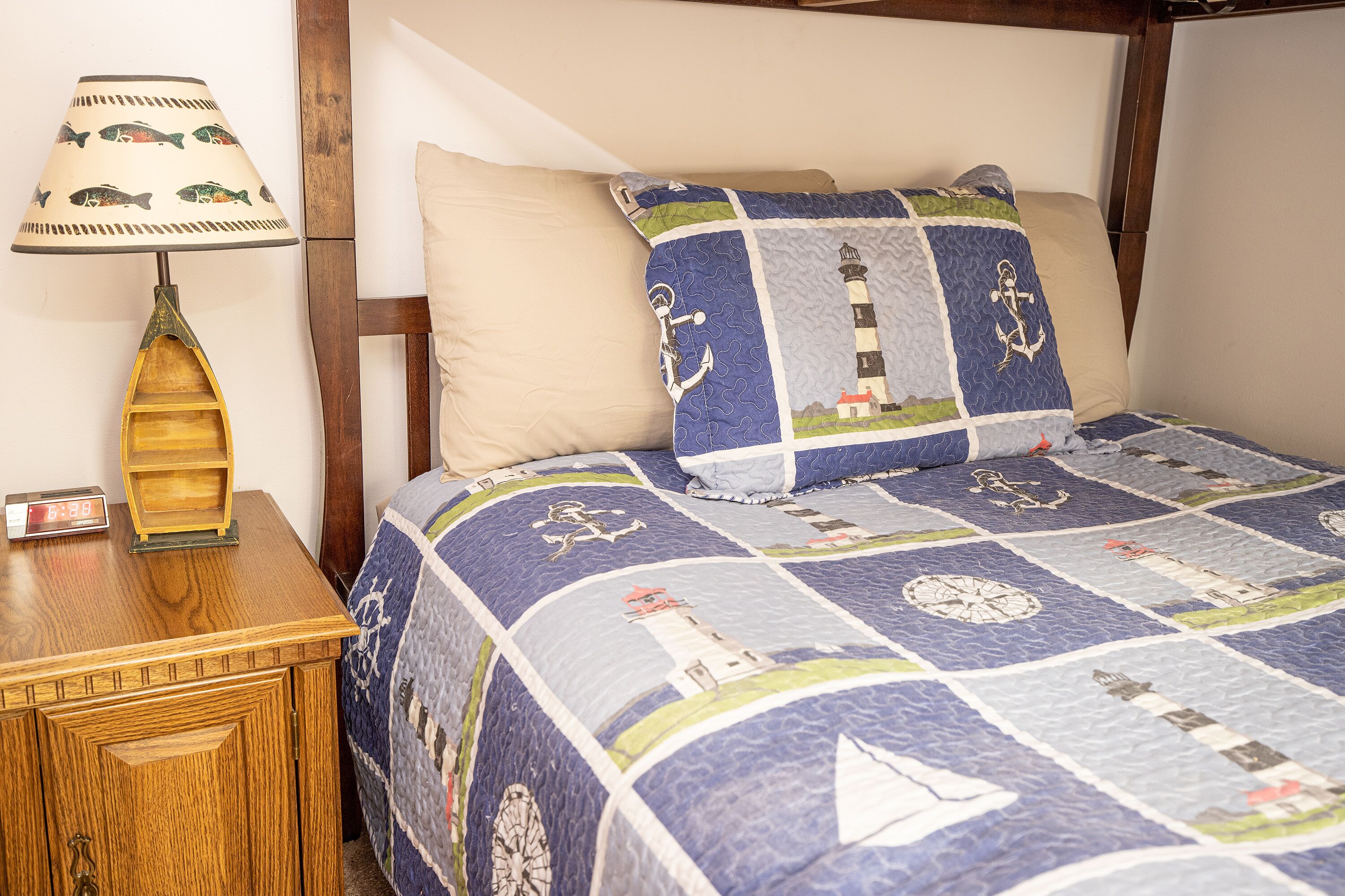 Una cama con colcha de temática náutica, una mesita de noche de madera con una lámpara y un pequeño reloj.
