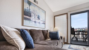 A living room with a brown sofa, a painting of boats, a table with chairs, and a view through a glass door. - Amazing Lakefront Pool On Coveted Horseshoe Bend! (Four Seasons)