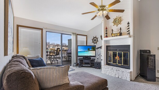 A living room with a large flat-screen TV, a fireplace, a ceiling fan, and a view of the outdoors through the sliding glass doors. - Amazing Lakefront Pool On Coveted Horseshoe Bend! (Four Seasons)