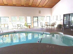 Une piscine intérieure dotée d’un plafond en bois, de grandes fenêtres et d’un espace extérieur aménagé pour se détendre.