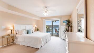 A bedroom with a bed, bedside lamps, a ceiling fan, a balcony with a view, and a dresser.