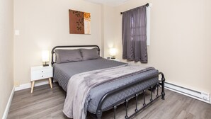 Een slaapkamer met een bed, nachtkastjes, een kunstwerk aan de muur en een raam met gordijnen.