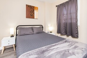 Ein Schlafzimmer mit Bett, Nachttischen, einem Wandbild und einem Fenster mit Vorhängen.