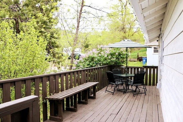 Eine Holzterrasse mit einer Bank und einem Tisch mit Stühlen, umgeben von Grünpflanzen und Bäumen.