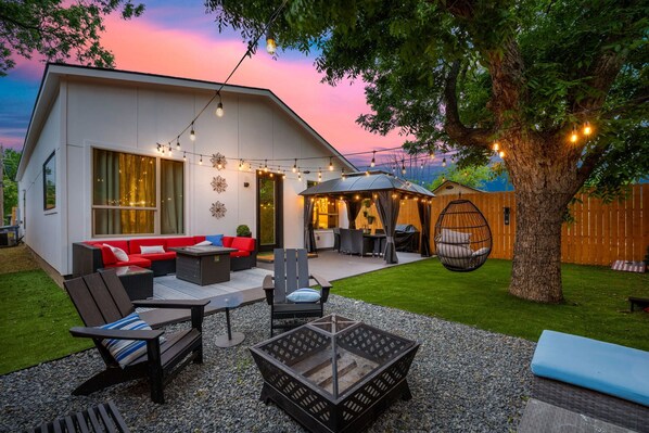 Una casa moderna con patio amoblado, que incluye mobiliario exterior, una mesa de vidrio y luces colgantes.