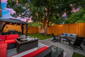Un patio exterior con un sofá rojo, mobiliario de mimbre negro y una silla colgante.