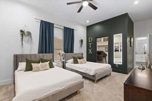 Un dormitorio moderno con dos camas, un ventilador de techo y una pared de acento oscura con las letras 'DTX'.