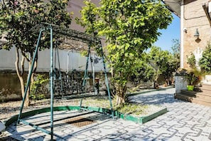 Relax on the patio surrounded by lush greenery and a stone wall, with a comfortable swing set to unwind.