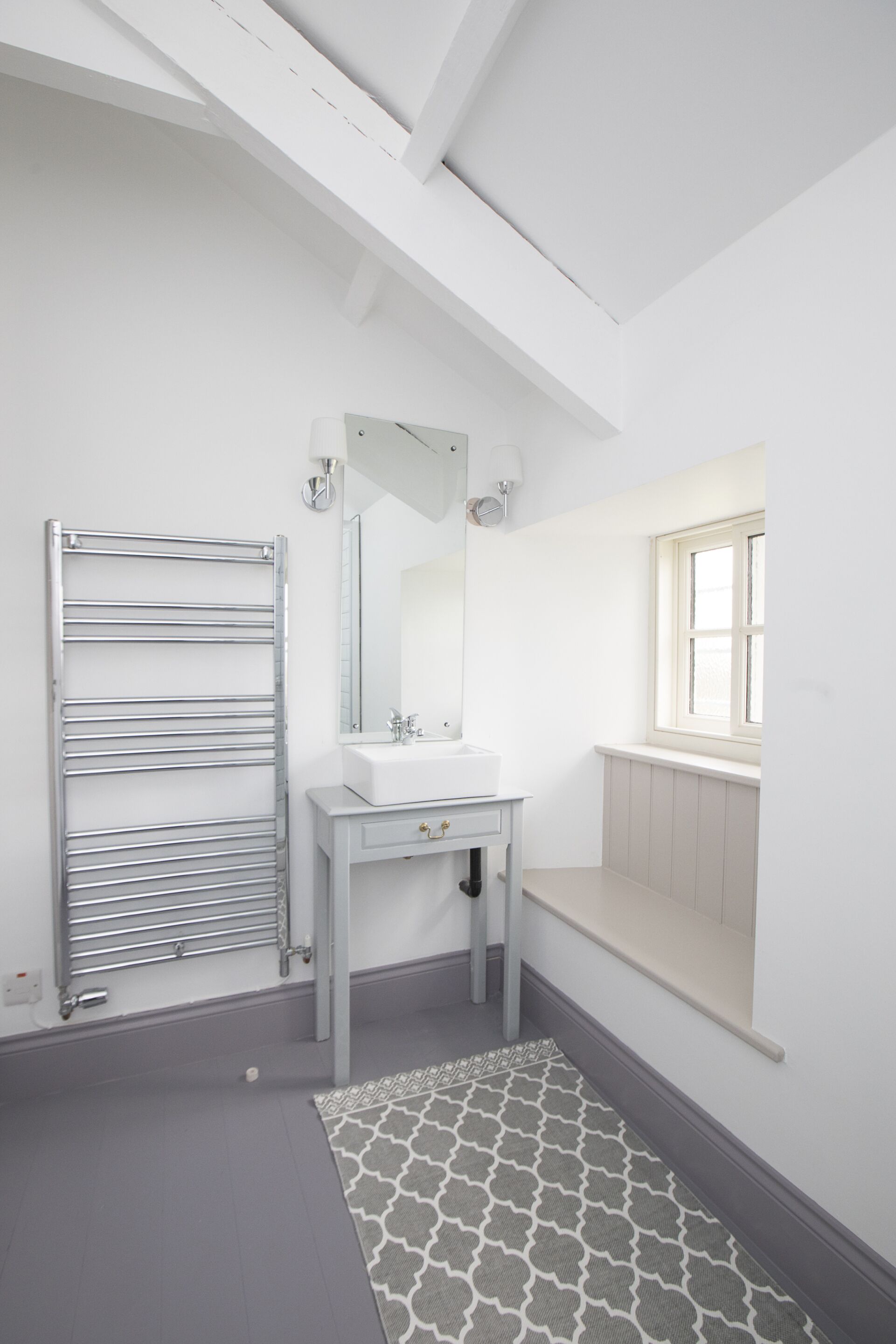 Un bagno con un mobile lavabo bianco, uno specchio, un portasciuga-asciugamani, una finestra e un tappeto decorato.