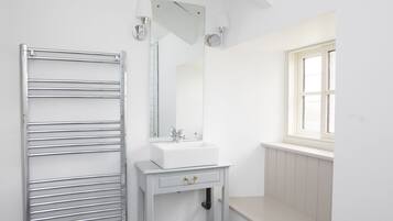 Un bagno con un mobile lavabo bianco, uno specchio, un portasciuga-asciugamani, una finestra e un tappeto decorato.