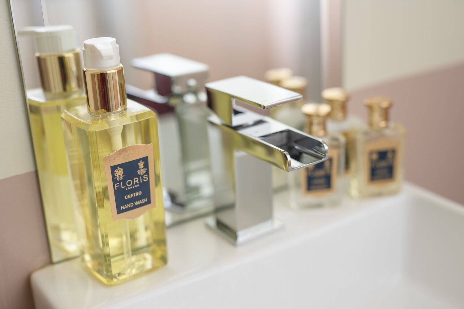A bathroom with a white sink, a mirror, and three bottles of hand wash soap.