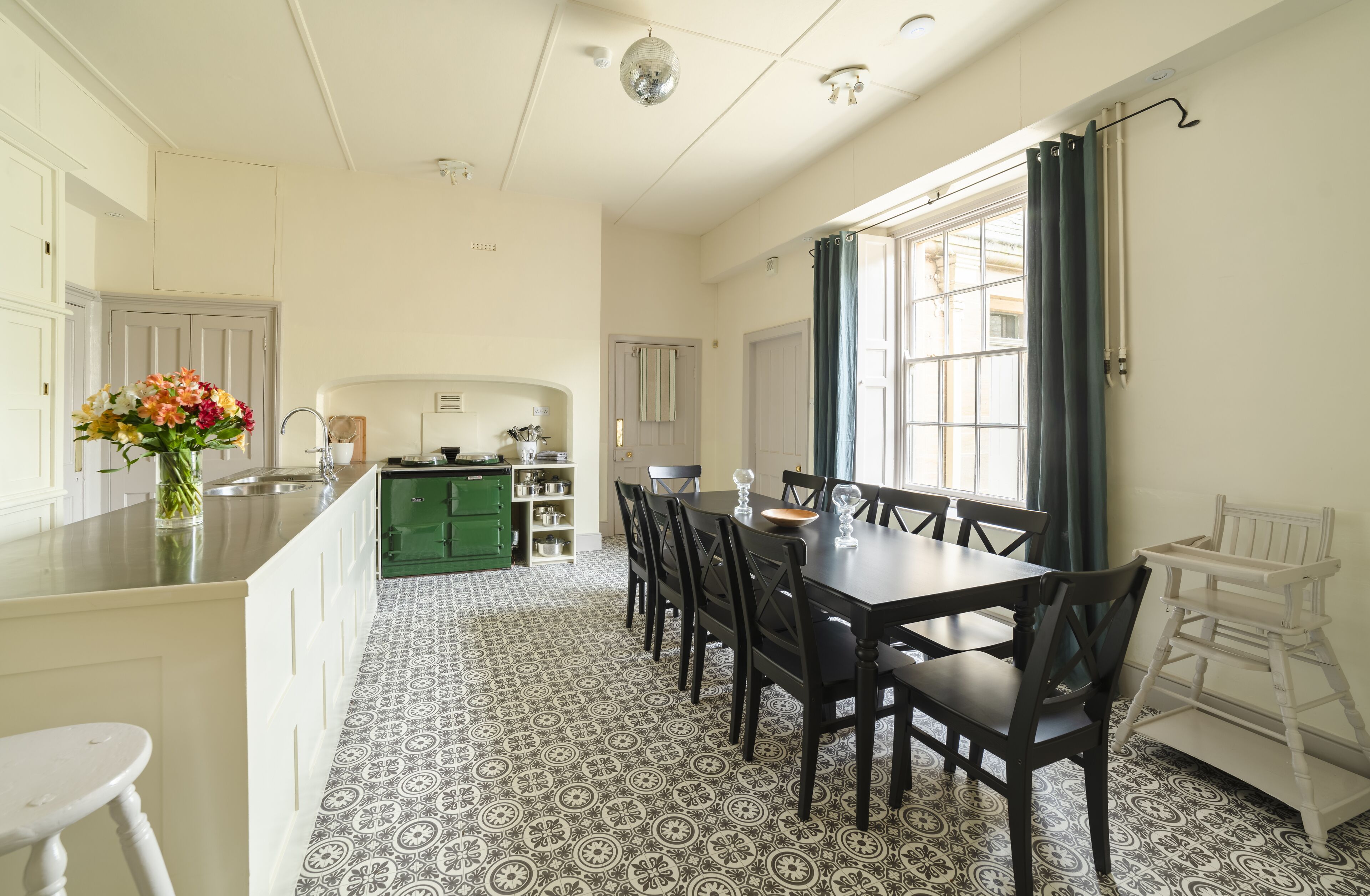 A spacious kitchen with a dining area, featuring a patterned floor, a green island, and a white chair.
