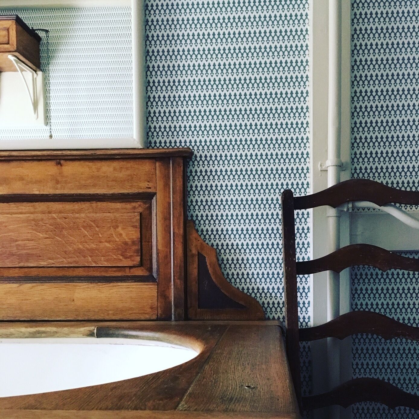 Una mesa de madera con superficie blanca, una silla de madera con respaldo curvo y papel tapiz estampado.