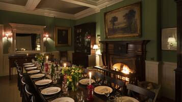Une salle à manger élégante, avec une longue table dressée pour un repas, une cheminée et un grand tableau encadré accroché au mur.