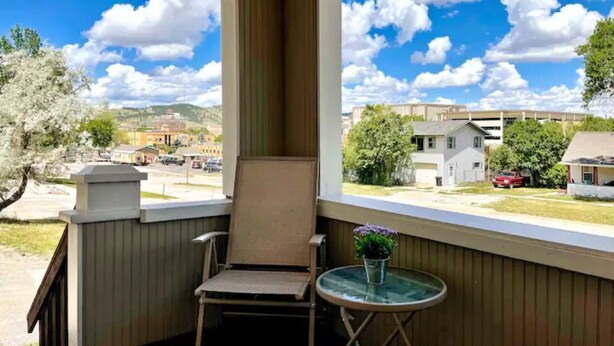 Ein Balkon mit Stuhl und kleinem Tisch, mit Blick auf ein Wohngebiet mit Häusern und blauem Himmel.