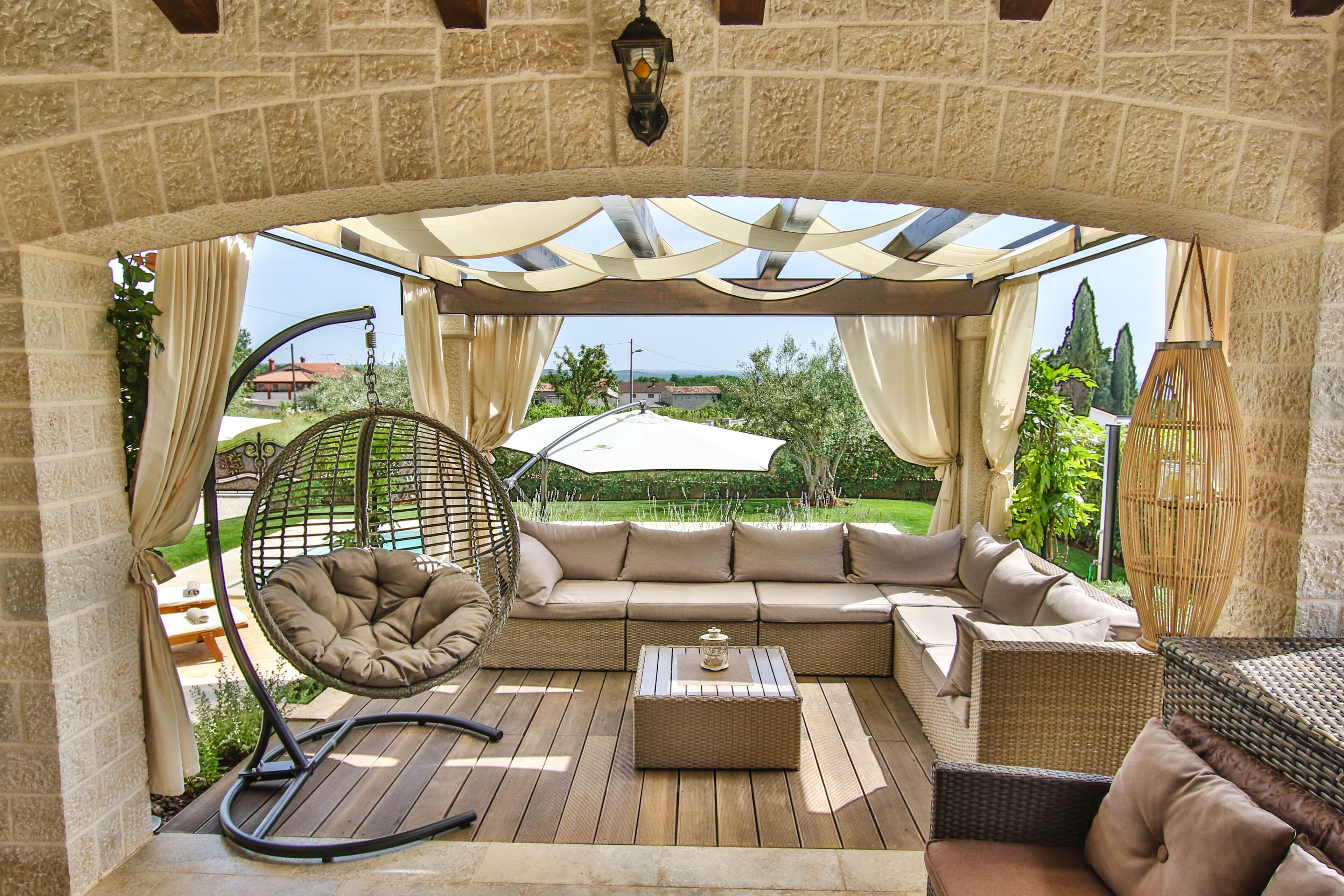 Un espacio al aire libre techado con un sofá de mimbre, una silla colgante y una mesa de madera.