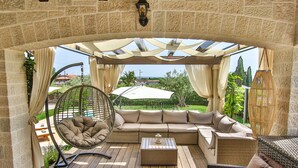 Un espacio al aire libre techado con un sofá de mimbre, una silla colgante y una mesa de madera.