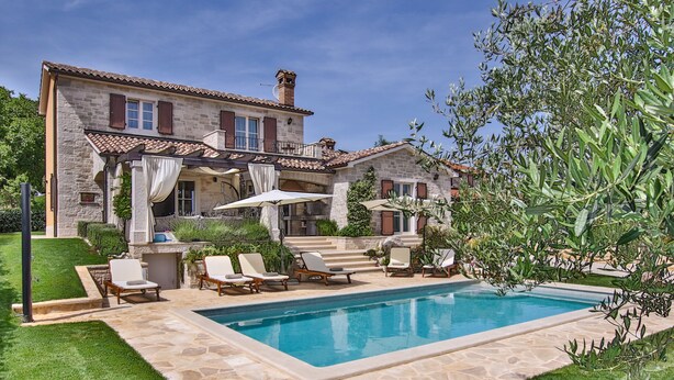 Una casa de piedra con piscina, mobiliario exterior y una pérgola.