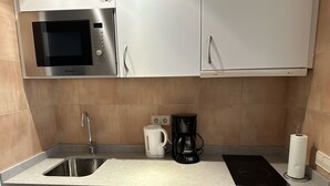 Ett kompakt kök med mikrovågsugn, kaffebryggare, vattenkokare och ett litet kylskåp.