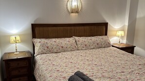 En snyggt bäddad säng med blommigt sänglinne, två sänglampor och en väggmonterad lampa.