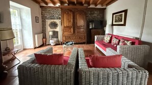 A living room with wicker furniture, a red sofa, and a stone fireplace. - CHEZ CONTOU 1 - GEUS-D'OLORON (GEUS-D'OLORON)