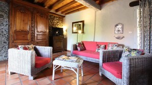 A cozy living room with wicker furniture, a red sofa, and a television. - CHEZ CONTOU 1 - GEUS-D'OLORON (GEUS-D'OLORON)