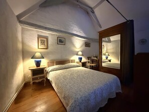 A bedroom with a bed, two bedside lamps, a wooden nightstand, a chair, a wooden door, and a mirror.