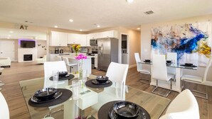 A modern kitchen with white cabinets, a central island, and a dining area with a glass table and white chairs.