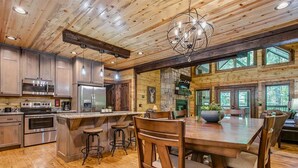 A spacious kitchen with wooden cabinets, stainless steel appliances, and a large island with stools. - Woodland Hot Tub Retreat for Families and Friends (Broken Bow)