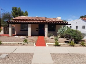 Una casa de una sola planta con techo de tejas rojas, un porche cubierto y un sendero rojo que lleva a la entrada.