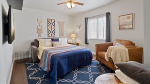 A bedroom with a bed, a sofa, a ceiling fan, a window with curtains, and wall decorations.