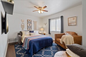 Un dormitorio con cama, sofá, ventilador de techo, ventana con cortinas y adornos en la pared.