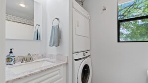 A modern bathroom with a built-in washing machine, a sink with a marble countertop, and a window with a view of trees.