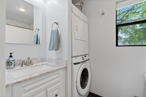 Un baño moderno con lavadora integrada, un lavabo con encimera de mármol y ventana con vistas a árboles.