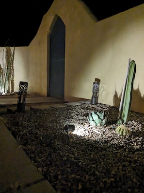 Espacio exterior nocturno con un cactus, una silla y una pared con una puerta.