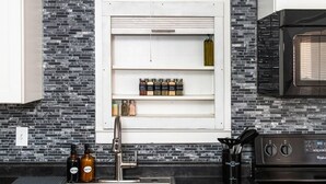 A kitchen with a black and white tiled backsplash, a built-in shelf with spices, a stainless steel sink, and a Whirlpool oven. - ⁂Centrally Located⁂Close to Downtown⁂Stocked Kitchen⁂ (Rapid City)