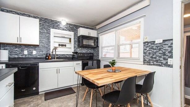 A modern kitchen with white cabinets, a black countertop, a wooden dining table, and black chairs. - ⁂Centrally Located⁂Close to Downtown⁂Stocked Kitchen⁂ (Rapid City)