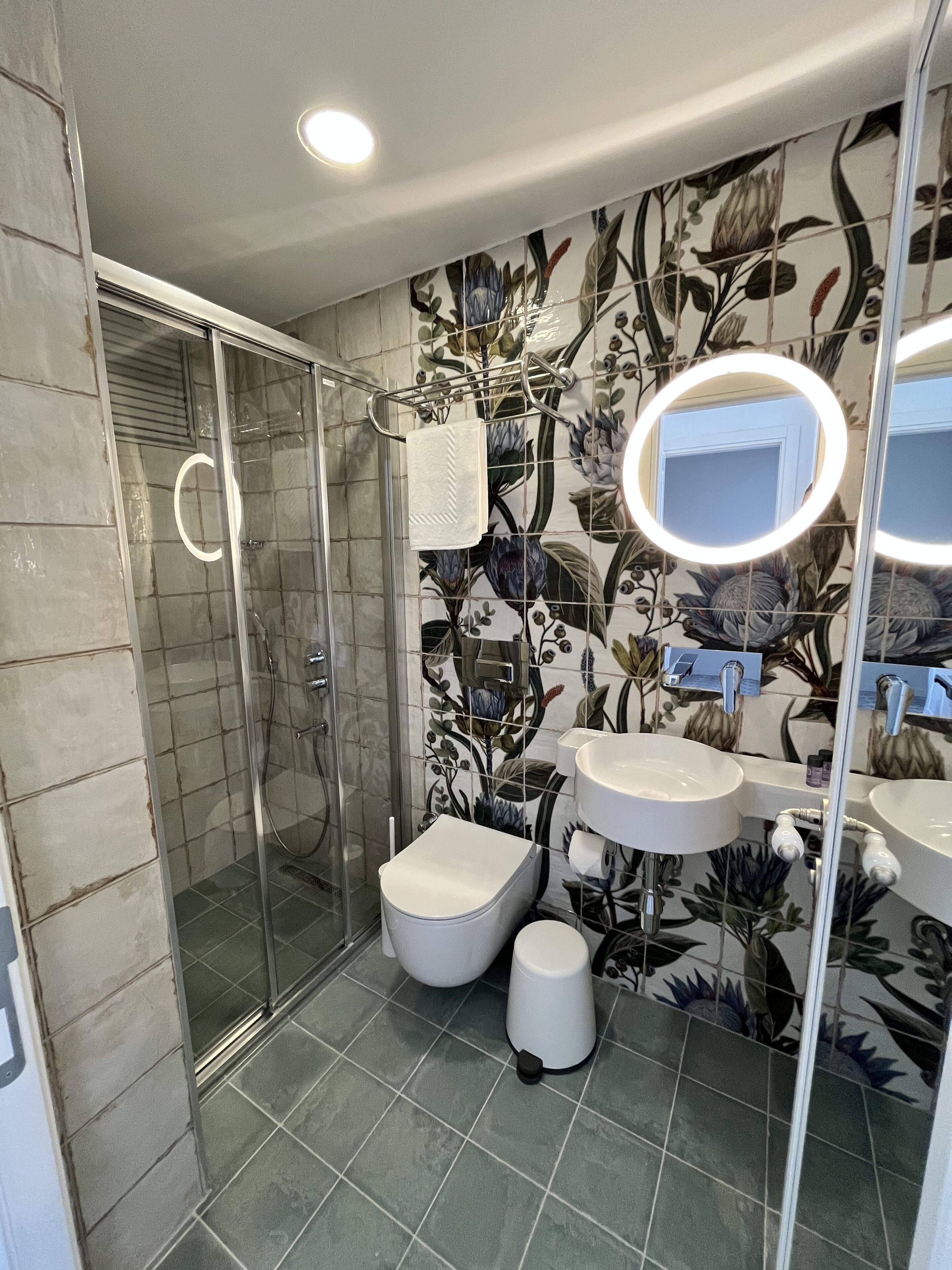 A bathroom with a glass shower enclosure, a toilet, a bidet, and a sink with a mirror.