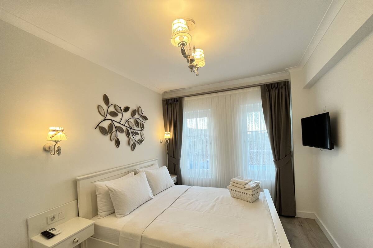 Una habitación de hotel con una cama grande, una mesita de noche con un teléfono, un televisor montado en la pared y un adorno en la pared.