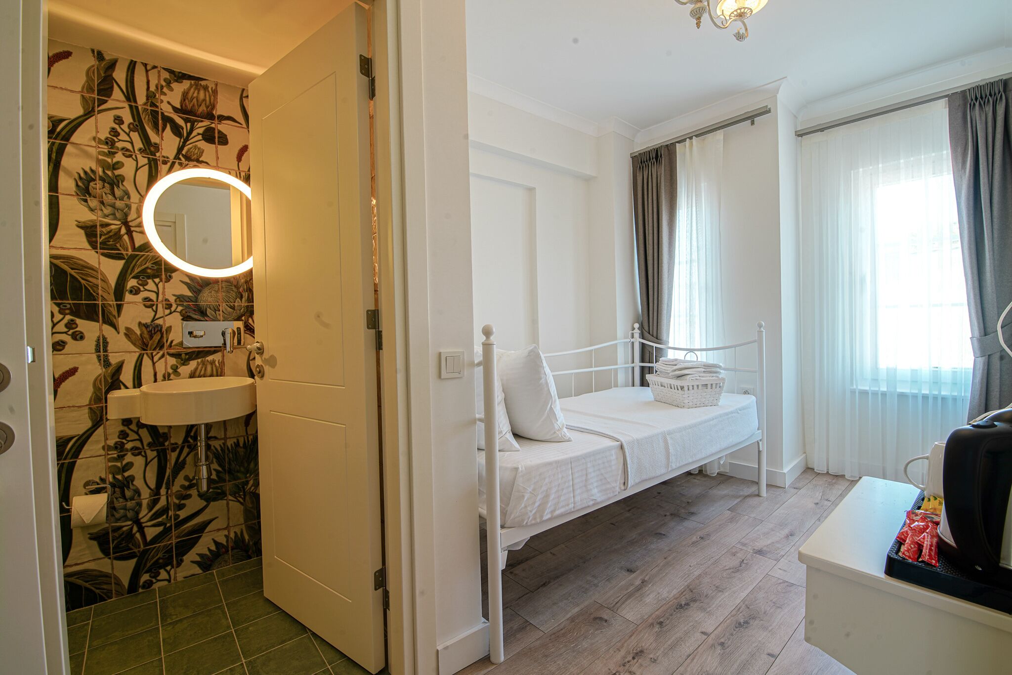 A room with a bed, a bedside table, a small sink, and a mirror with a light.