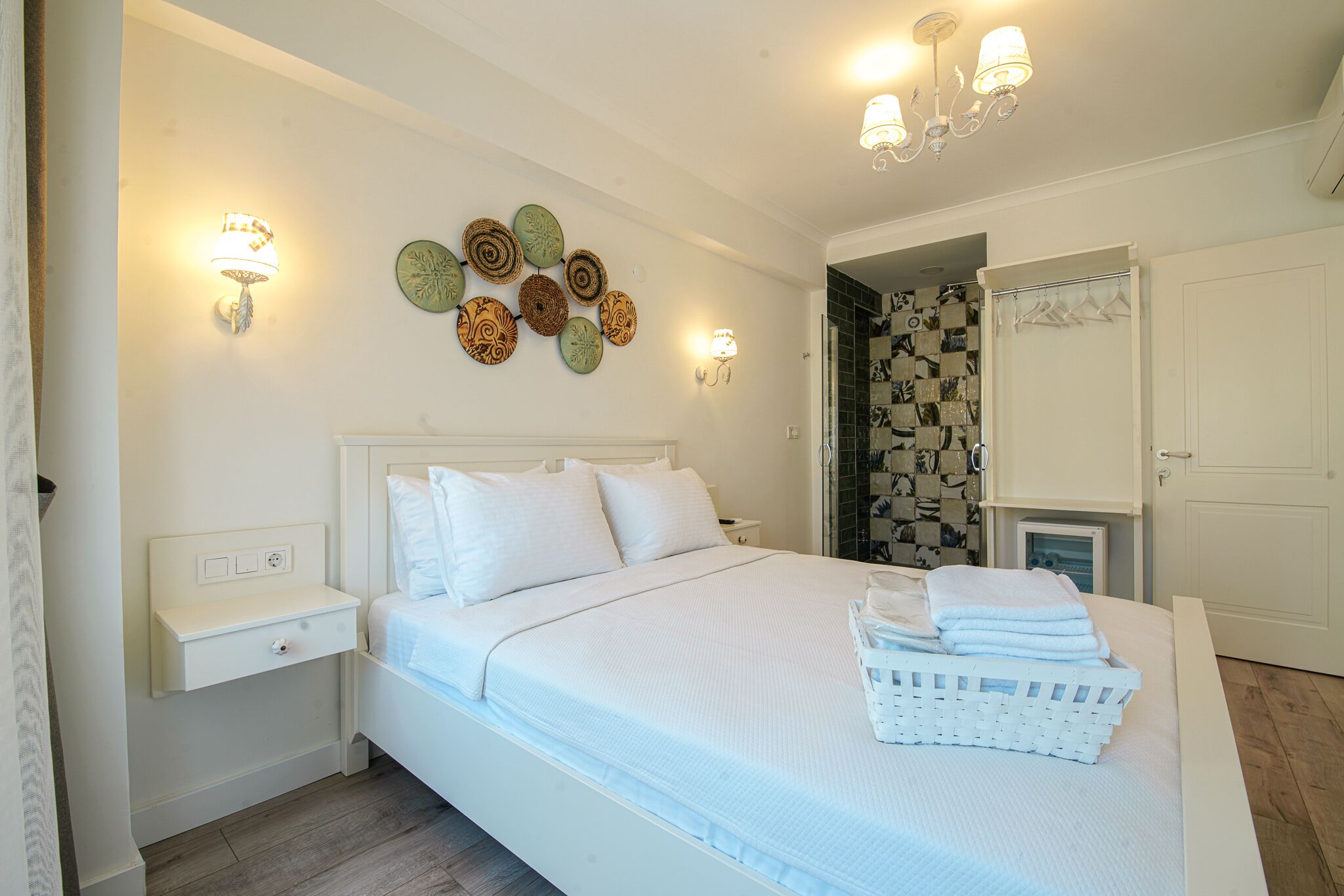 A neatly arranged bedroom with a large bed, bedside tables, wall-mounted lights, and a door leading to a bathroom.