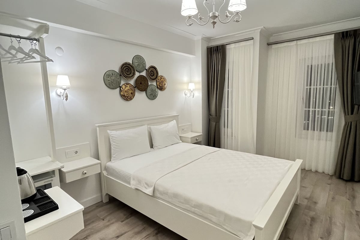 Un dormitorio moderno con una cama grande, mesitas de noche, un espejo, apliques de pared y una araña.