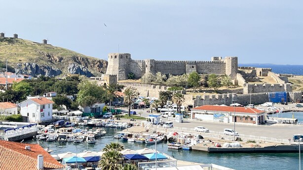 A coastal town with a historic fort, a marina with boats, and buildings with red-tiled roofs. - Mavrella Bozcaada (Bozcaada)
