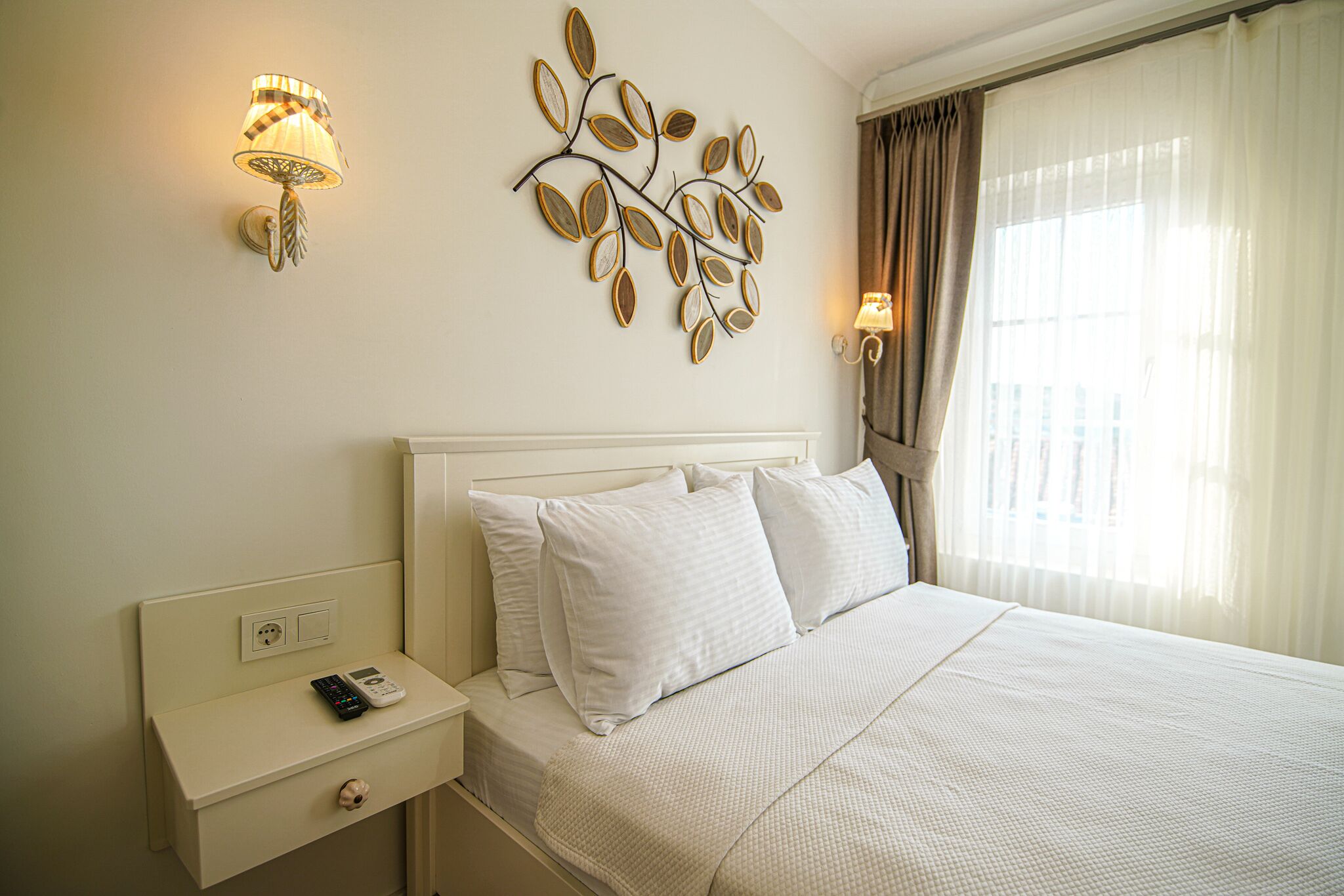 A neatly made bed with white linens, a bedside table with a lamp, and a wall-mounted decorative piece.