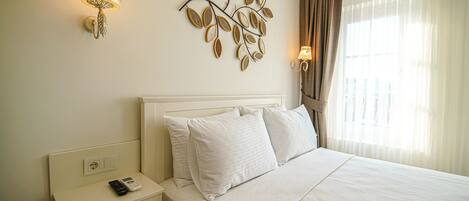 A neatly made bed with white linens, a bedside table with a lamp, and a wall-mounted decorative piece.