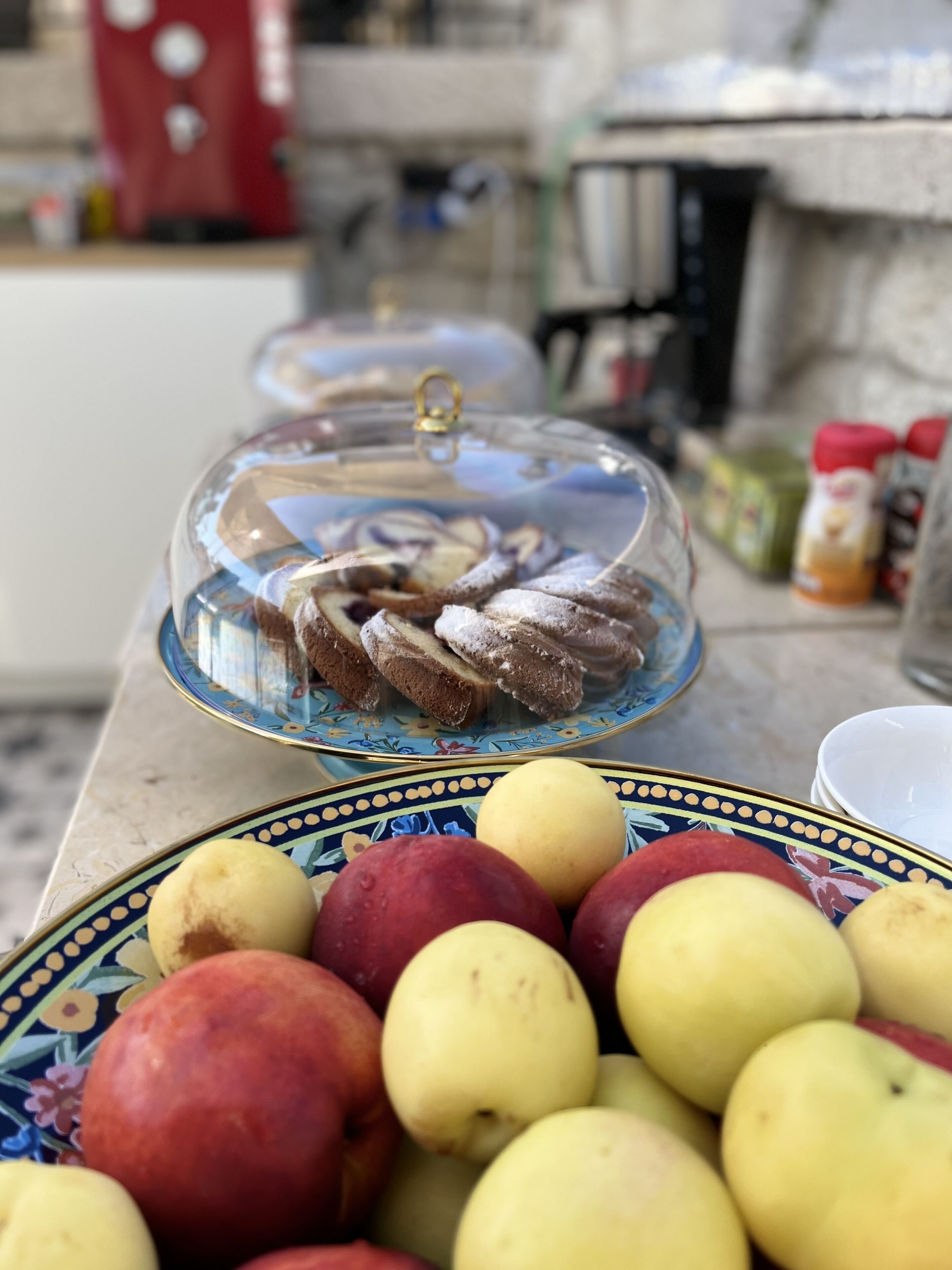 A table with a glass dome containing pastries and a plate of apples.