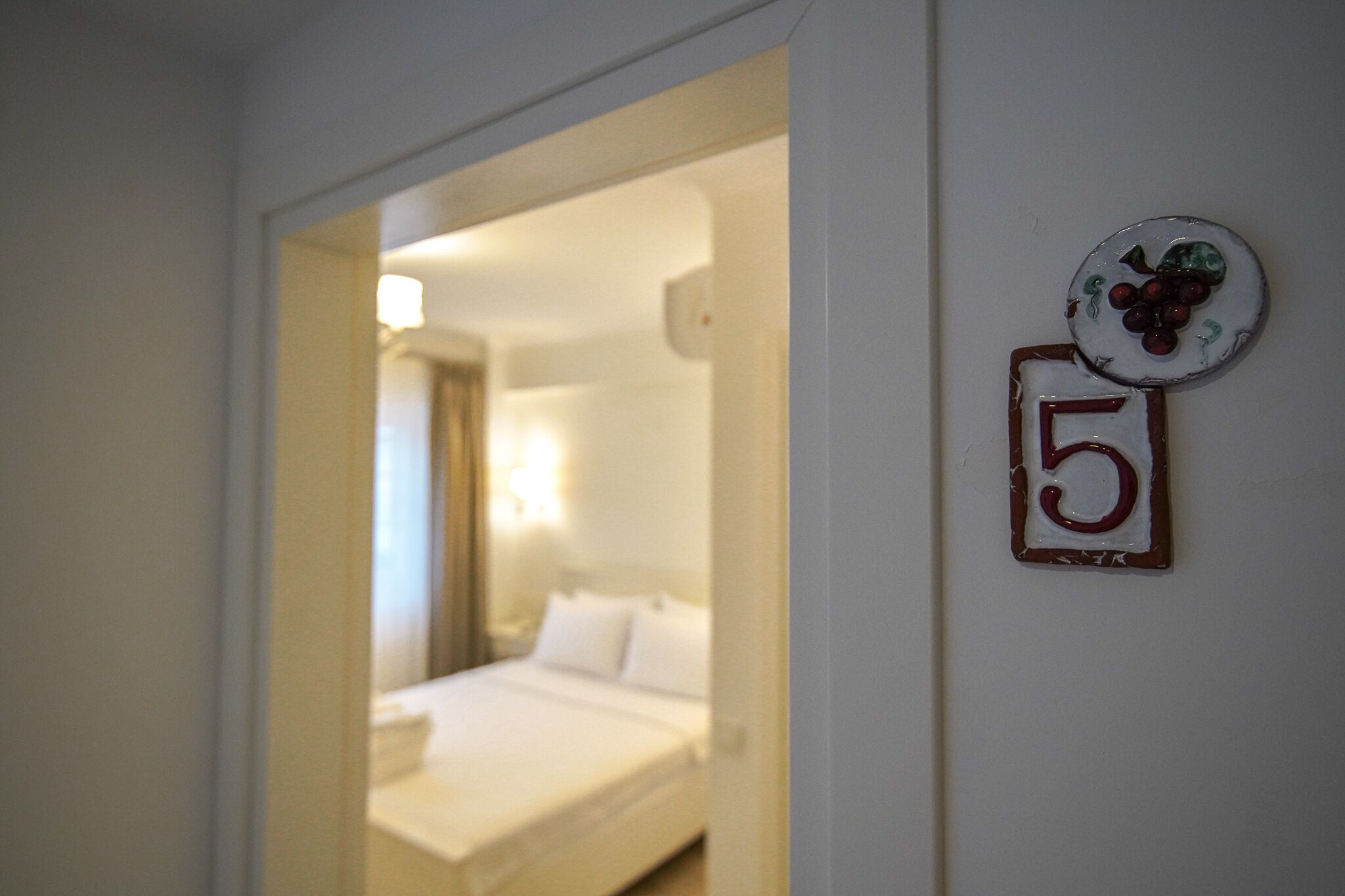 A hotel room with a bed, a nightstand, and a wall-mounted number '5'.
