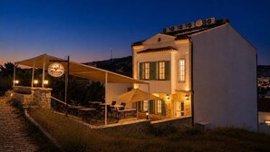 A white building with a covered outdoor seating area, a sign reading 'Mavrella Bostado,' and a stone wall. - Mavrella Bozcaada (Bozcaada)