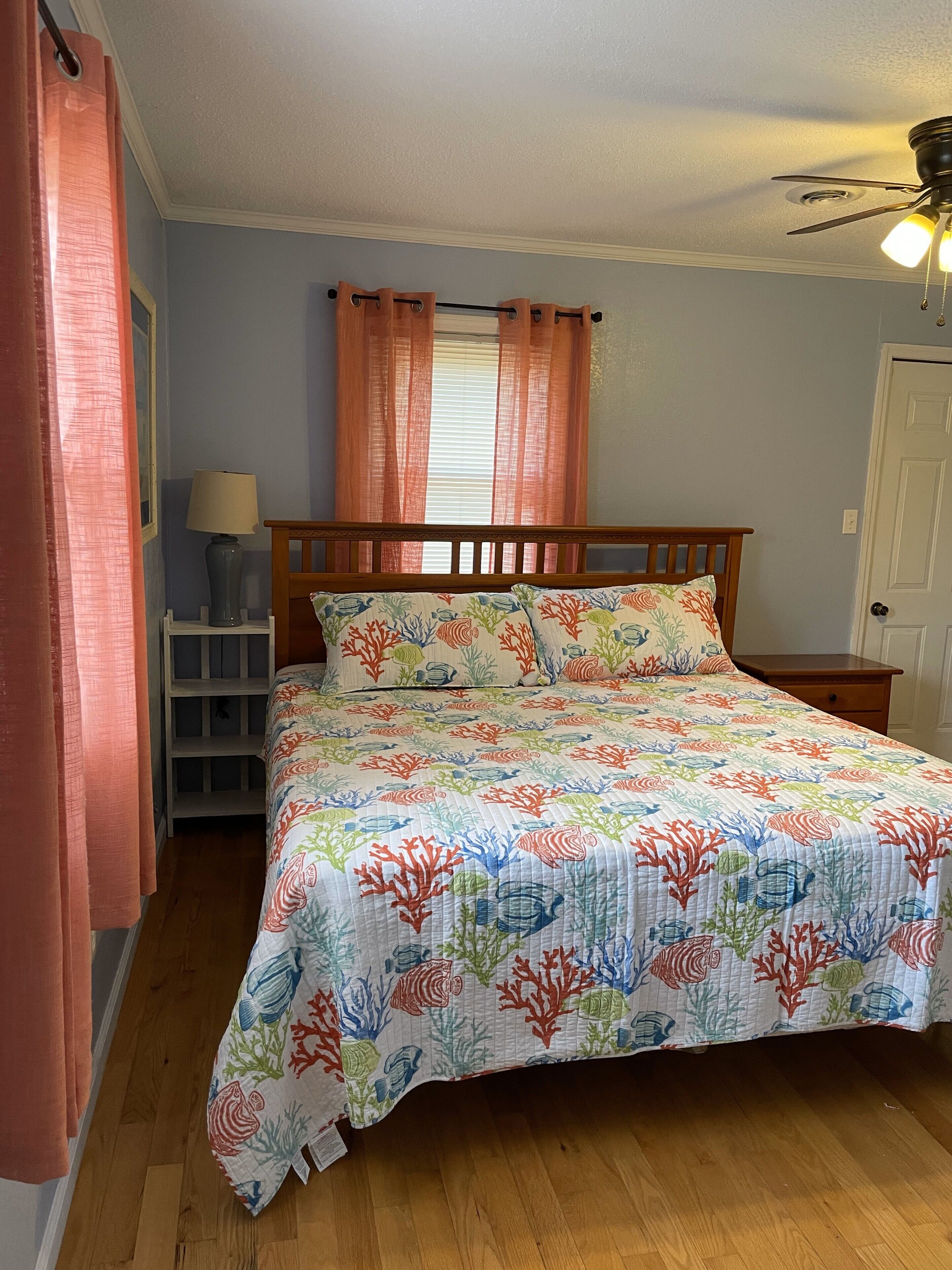 A bedroom with a bed, a nightstand, a lamp, a ceiling fan, and a window with curtains.